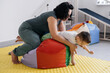 Therapist doing exercises on the mat with disabled child. Boy with cerebral palsy having rehabilitation on the ball, bag. Spine and neck, foots training on the floor of center 