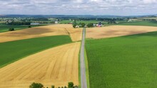 Rising Aerial. Road Cuts Through American Farmland. Summer Fields Of Wheat, Grain, Green Alfalfa Hay. Beautiful Rolling Hills, Cloud Shadows.