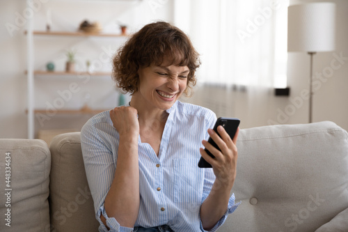 Joyful emotional young woman looking at smartphone screen, celebrating online lottery gambling betting auction win, making yes gesture reading email with amazing win news, internet success concept.