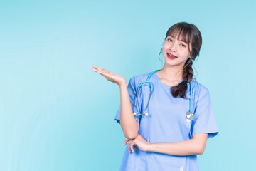 Happy smiling with Braces young Asian female doctor hand pointing present showing, medical health care worker surgeon specialist in uniform scrub with stethoscope, copy space blue isolated background