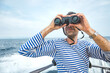 © Aleksandra - young man, sailor in striped jacket - vest with stubble sits on boat in sea and looks ahead through binoculars. sea navigation, summer tourism. travel content, selective focus