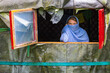 Young blue-eyed girl with headscarf leaning out of the window of a Mongolian tent.