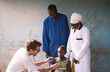 Multiethnic medical staff in blue and white labcoats during lung examination on a shy little schoolgirl in a Western African hospital