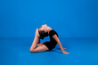 a small gymnast in a black swimsuit does flexibility exercises on a blue background with a copy of the space