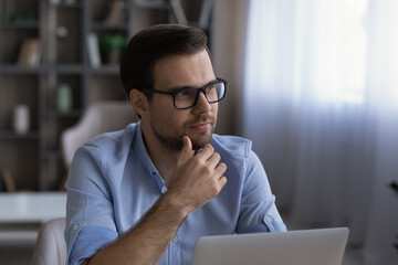 Poster - Visualizing work. Pensive young man entrepreneur wear glasses work at laptop online look aside think create business plan ponder on idea. Thoughtful millennial male consider on important issue at pc