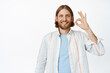 © Cookie Studio - Handsome blond man with beard showing okay sign, standing in white shirt against studio background