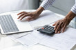 © fizkes - Crop close up of African American woman calculate expenses expenditures on machine pay bills on computer online. Ethnic female manage household budget on laptop, consider financial banking paperwork.