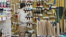 Slowmo shot of young man with shopping bag choosing paintbrush and paint roller at hardware store
