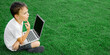 © vovan - child sits on the grass and studies with a laptop online, enjoying nature