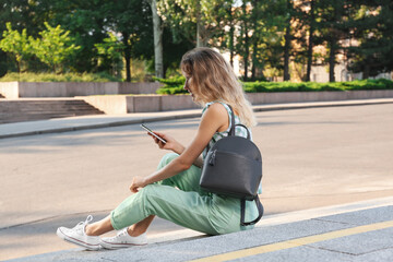 Wall Mural - Young woman with stylish backpack and smartphone on stairs outdoors