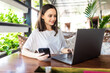 © dianagrytsku - Freelance young woman sitting in the cafeteria with laptop and drinking coffee while use her phone