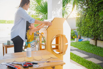 Children kids girls and mother hand making  paper house at home. Asian little child girl make and playing with cardboard house with her mom.