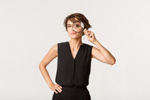 Intrigued Stylish Woman Looking Through Magnifying Glass, Smiling Thoughtful, Standing Over White Background