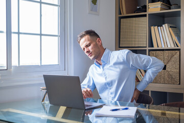 Close up rear view stressed young man touching lower back feeling discomfort, suffering from sudden pain due to sedentary lifestyle or long computer overwork in incorrect posture at home office..