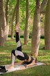 © CristianUrriaga - Vertical image of a young woman doing a pilates pose while she records herself with her tablet relaxing outdoors in the park. Concept of outdoor pilates.