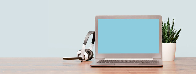 Wall Mural - Laptop. Mockup screen and headphones on wooden desk and plain background banner. Distant learning. working from home, online courses or support minimal concept. Helpdesk or call center headset