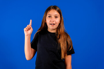 Wall Mural - Pretty hispanic preteen girl raising her index finger while smiling, voluntarily lending herself to take action. Positive attitude. Will concept