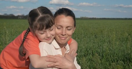 woman and child sits in the wheat. a little girl warmly embrace her mother in the green field in cou