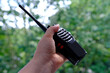 close-up female hand holds black gadget, portable radio station, receiving-transmitting device designed for operational communication on natural background, concept of modern technologies in forest