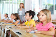 © JackF - Schoolchildren sitting at desks in classroom. Female teacher staning beside desks.