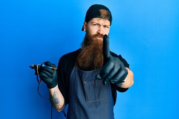 Wall Mural - Redhead man with long beard tattoo artist wearing professional uniform and gloves pointing with finger up and angry expression, showing no gesture