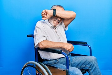 Poster - Handsome senior man with beard sitting on wheelchair smiling cheerful playing peek a boo with hands showing face. surprised and exited