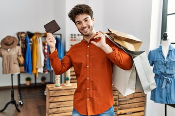 Wall Mural - Young hispanic customer man smiling happy holding shopping bags and leather purse at clothing store.