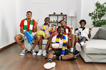 Canvas Print - Young african men wearing team scarf cheering football game smiling happy pointing with hand and finger to the side