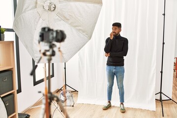 Wall Mural - Young hispanic man with beard posing as model at photography studio looking stressed and nervous with hands on mouth biting nails. anxiety problem.