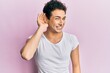© Krakenimages.com - Young handsome man wearing casual white t shirt smiling with hand over ear listening an hearing to rumor or gossip. deafness concept.