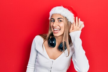 Poster - Beautiful hispanic woman wearing christmas hat and headphones smiling with hand over ear listening and hearing to rumor or gossip. deafness concept.