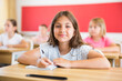 Schoolchildren sitting at desks in classroom. Young girl looking in camera.