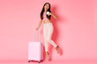Travelling, holidays and vacation concept. Full-length of silly and glamour asian girl in summer clothes jumping happy with passport and flight tickets, carry suitcase to airplane, pink background