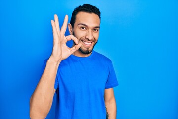 Hispanic man with beard wearing casual blue t shirt smiling positive doing ok sign with hand and fingers. successful expression.