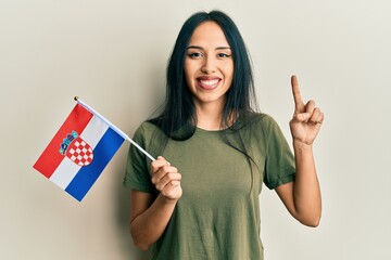 Wall Mural - Young hispanic girl holding croatia flag smiling with an idea or question pointing finger with happy face, number one