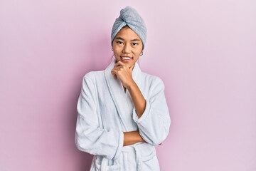 Poster - Young chinese woman wearing shower towel cap and bathrobe looking confident at the camera smiling with crossed arms and hand raised on chin. thinking positive.