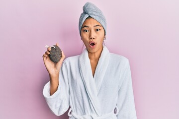 Poster - Young chinese woman wearing shower towel cap and bathrobe holding pumice stone scared and amazed with open mouth for surprise, disbelief face