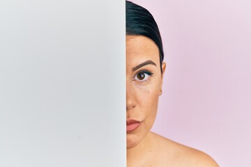 Poster - Beautiful brunette woman holding blank empty banner covering half face relaxed with serious expression on face. simple and natural looking at the camera.