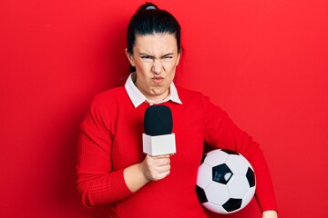 Sticker - Young hispanic woman holding reporter microphone and soccer ball skeptic and nervous, frowning upset because of problem. negative person.