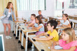 © JackF - Focused preteen pupils studying in classroom with female teacher, writing exercises in workbooks..