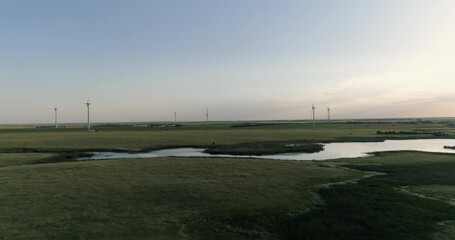 Wall Mural - Aerial above green meadows and water pond towards highway and wind turbines. Sunset warm sky, South Dakota