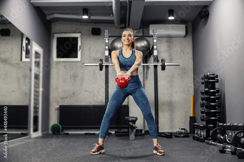 Swing exercise and dead lift dumbbells to burn the muscles of the buttocks and legs. A front view of a sexy woman in sportswear and in good physical shape lifting weights in an indoor gym