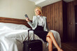 © Dusan Petkovic - End of a business trip. Beautiful and successful woman in formal clothes is sitting on the bed in a hotel room and using a phone. Next to her is a black suitcase she prepares to check out of the hotel