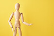 Wooden doll with gesture on yellow background. Mannequin shows gesture. Figure of wooden human with copy space