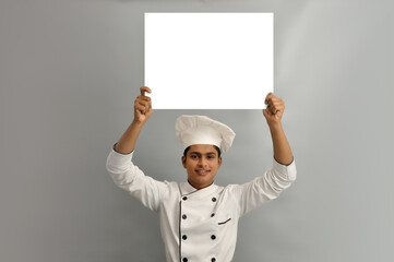 Happy male chef dressed in uniform holding white advertising banner, good poster for ad, offer or announcement, big paper billboard