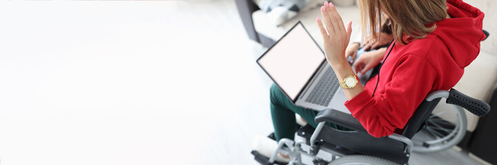 Disabled woman in wheelchair waving hand at laptop screen