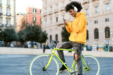Happy African Man Using Mobile Smartphone Outdoor - Young Guy Having Fun Riding With Bike In The City - Youth Millennial Generation Lifestyle And Technology Concept