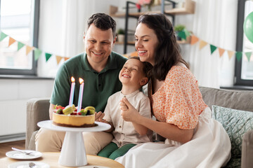 Wall Mural - family, holidays and people concept - portrait of happy mother, father and little son with four candles on birthday cake sitting on sofa at home party