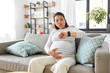 © Syda Productions - pregnancy, rest, people and expectation concept - pregnant asian woman with smart watch having labor contractions sitting on sofa at home and breathing