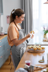 Wall Mural - culinary, bake and cooking food concept - happy smiling young woman with baking bag making cupcake topping on kitchen at home